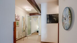 A hallway with a wooden ceiling, a white radiator, a glass door, and a wall with a chalkboard and a clock. - Apartment Charles Bridge (Prague)