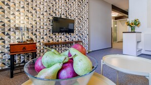 A modern room with geometric patterned wallpaper, a flat-screen TV mounted on the wall, a wooden side table, and a glass bowl of fruit on a tray. - Apartment Charles Bridge (Prague)