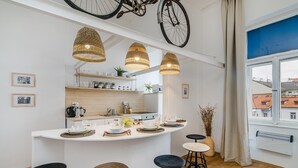 A modern kitchen with a central island, bar stools, hanging bicycle wheels as decor, and a view of buildings through a large window. - Historic Centre APTs by Michal&Friends (Prague)
