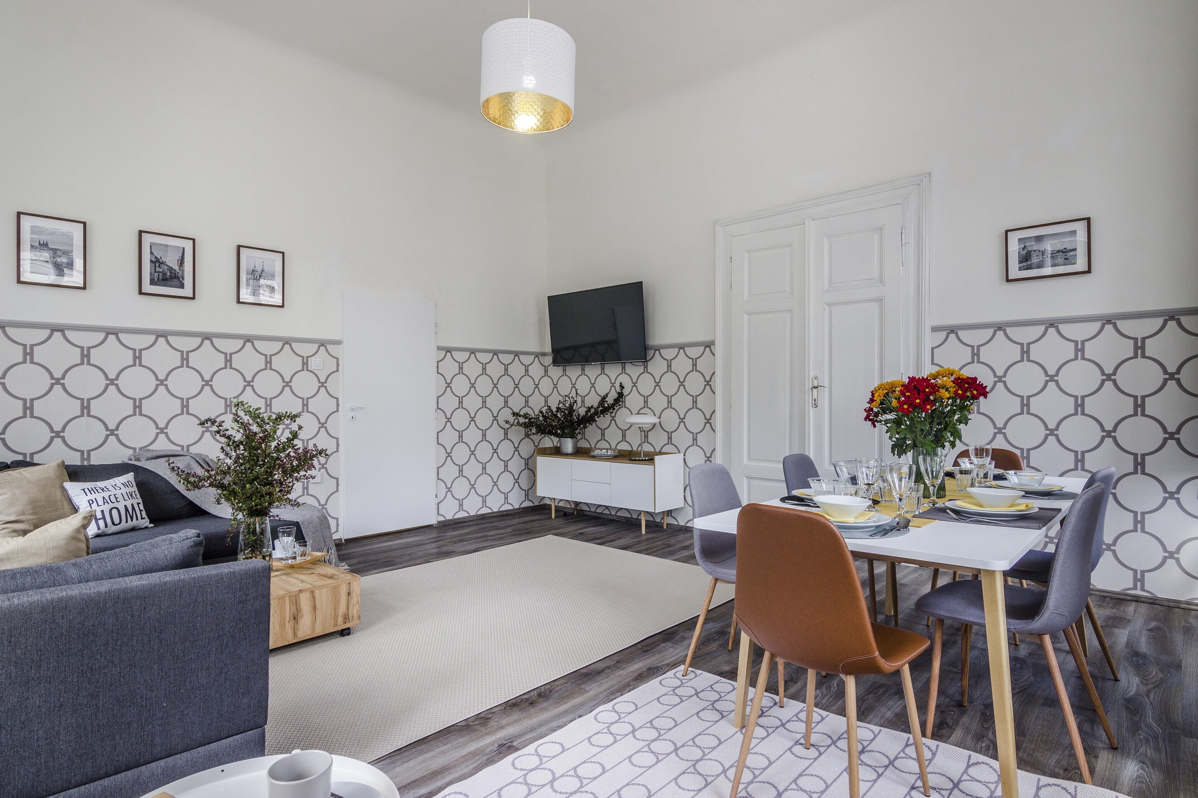 Ein modernes Wohnzimmer mit einem grauen Sofa, einem Esstisch für vier Personen und einem an der Wand befestigten Fernseher.