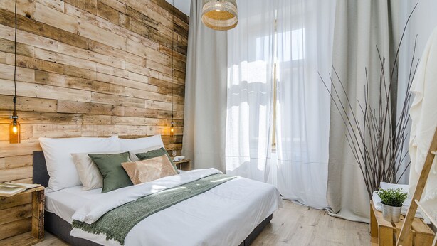 A bedroom with a wooden wall, a bed with white bedding, a hanging light fixture, and a window with sheer curtains. - Historic Centre APTs by Michal&Friends (Prague)