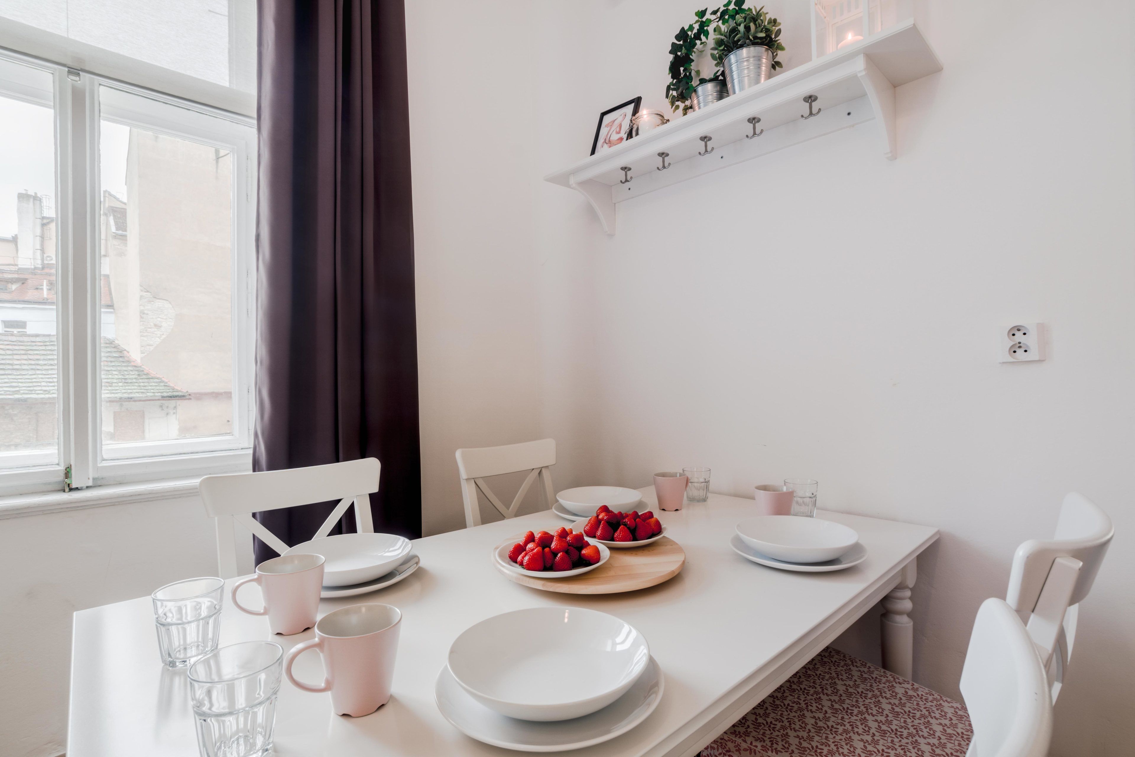 A dining area with a white table, chairs, and a shelf with decorative items.