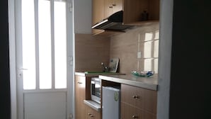 A compact kitchen with wooden cabinets, a built-in oven, and a refrigerator. - Akropolis Studios (Agios Vasileios)
