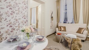 Un comedor con una mesa redonda dispuesta para una comida, un sofá con cojines, una ventana con cortinas y un espejo en la pared.