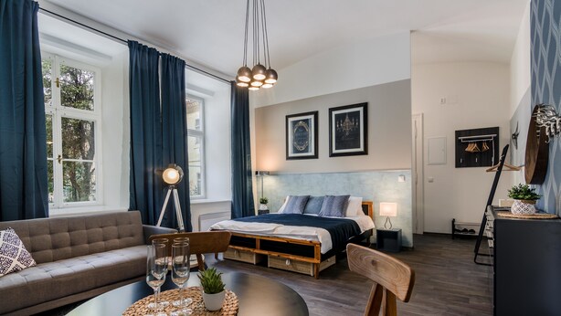 Una habitación de hotel moderna con sofá, una mesa de comedor con vasos, una cama con cabecero y un escritorio con lámpara.