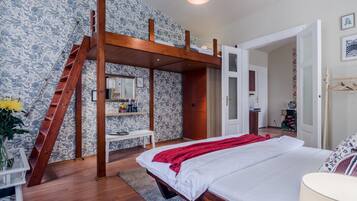 A bedroom with a bunk bed, wooden ladder, a bedside table with a vase of flowers, a bedside lamp, and a wardrobe.