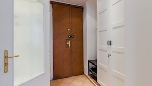 Un pasillo con una puerta de madera cerrada, una puerta blanca con un panel de vidrio satinado y un armario blanco con estante.