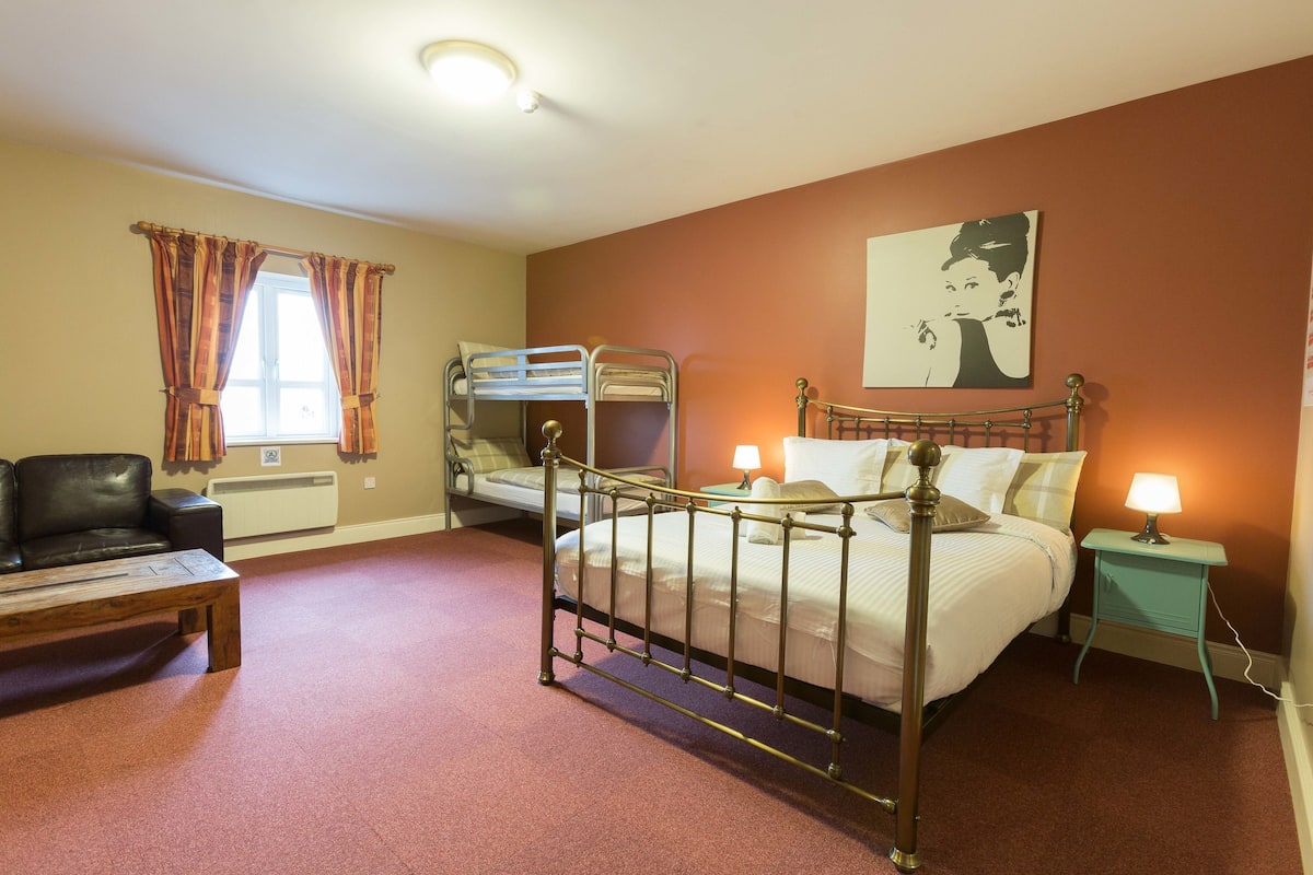 A hotel room with a bunk bed, a desk, a chair, a lamp, and a painting on the wall.