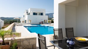 A modern pool area with a clear view of a white building and a dining table with chairs. - Triton Sea View 7 - two bedroom house close to the sandy beach (Asprouliani)