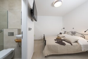 A modern bedroom with a bed, a TV mounted on the wall, and a bathroom with a toilet and sink. - Hvar Villa Maris (Hvar)