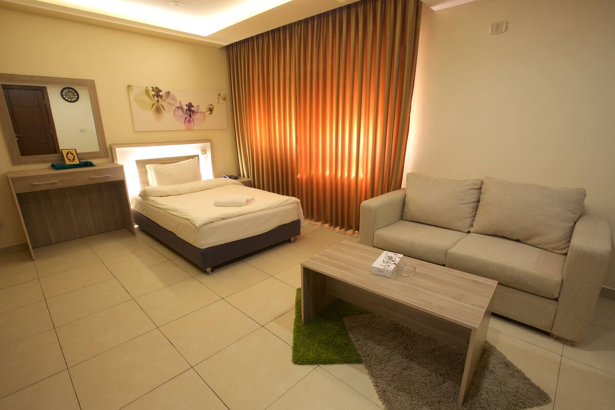 A hotel room with a bed, a sofa, a desk, and a mirror.