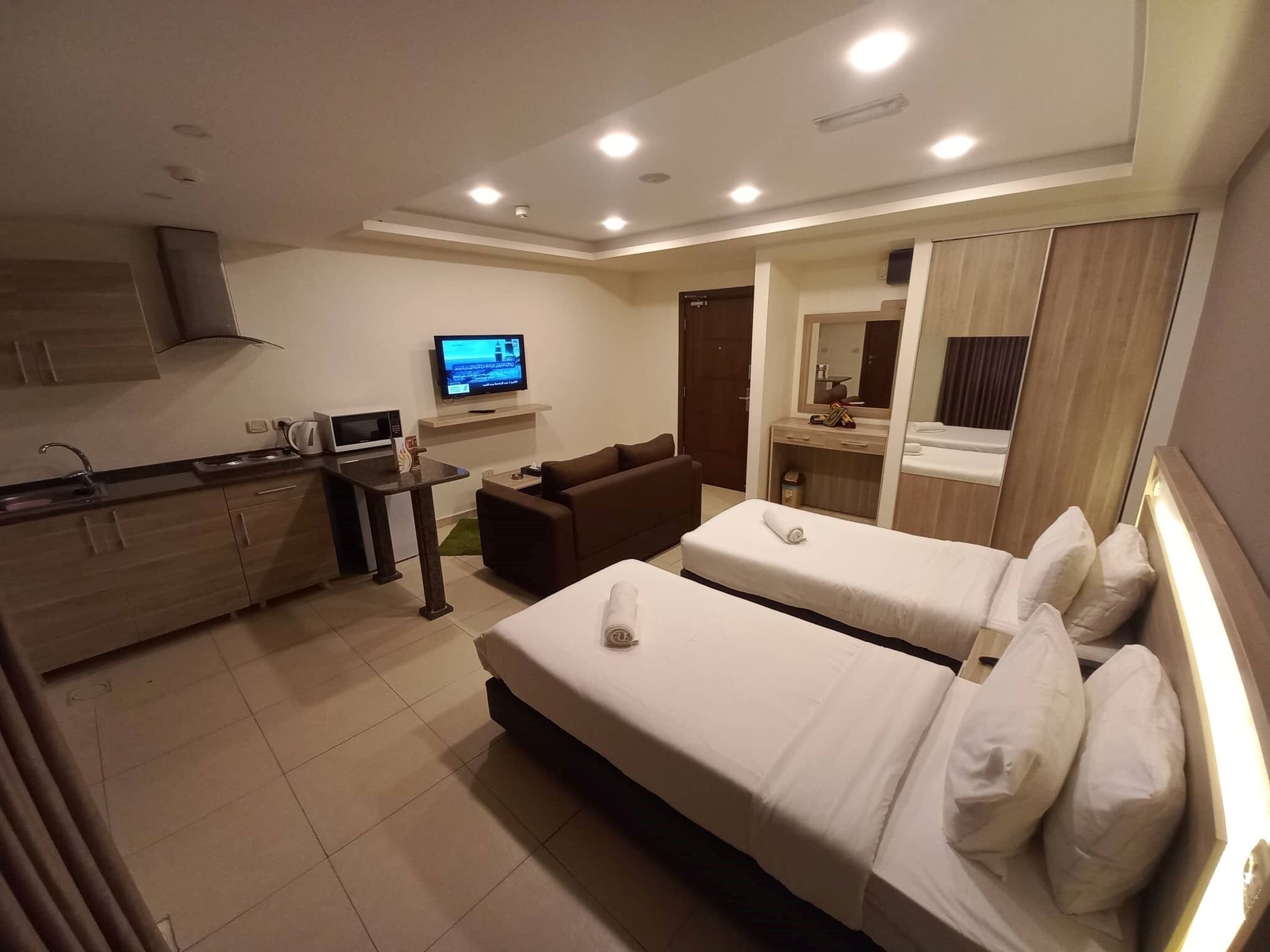 Habitación de hotel con dos camas, kitchenette, televisión y baño.