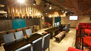 A modern dining area with a long table, blue chairs, and red sofas. - Lujain Hotel Suites (Amman)