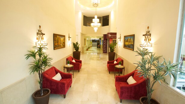 A hotel lobby with a chandelier, red chairs, potted plants, and artwork on the walls. - Lujain Hotel Suites (Amman)