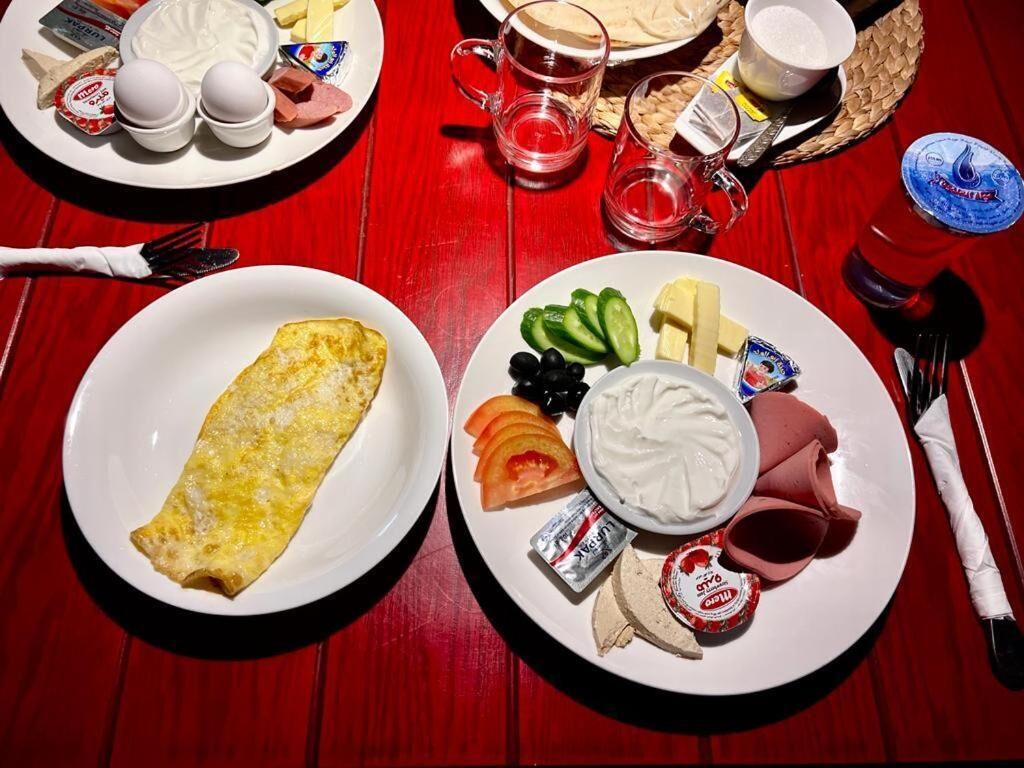 A breakfast setting with plates of food including an omelette, cheese, tomatoes, cucumbers, and yogurt.