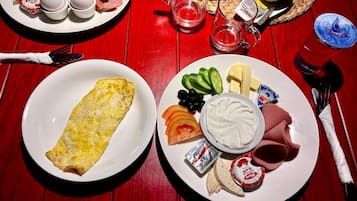 A breakfast setting with plates of food including an omelette, cheese, tomatoes, cucumbers, and yogurt.