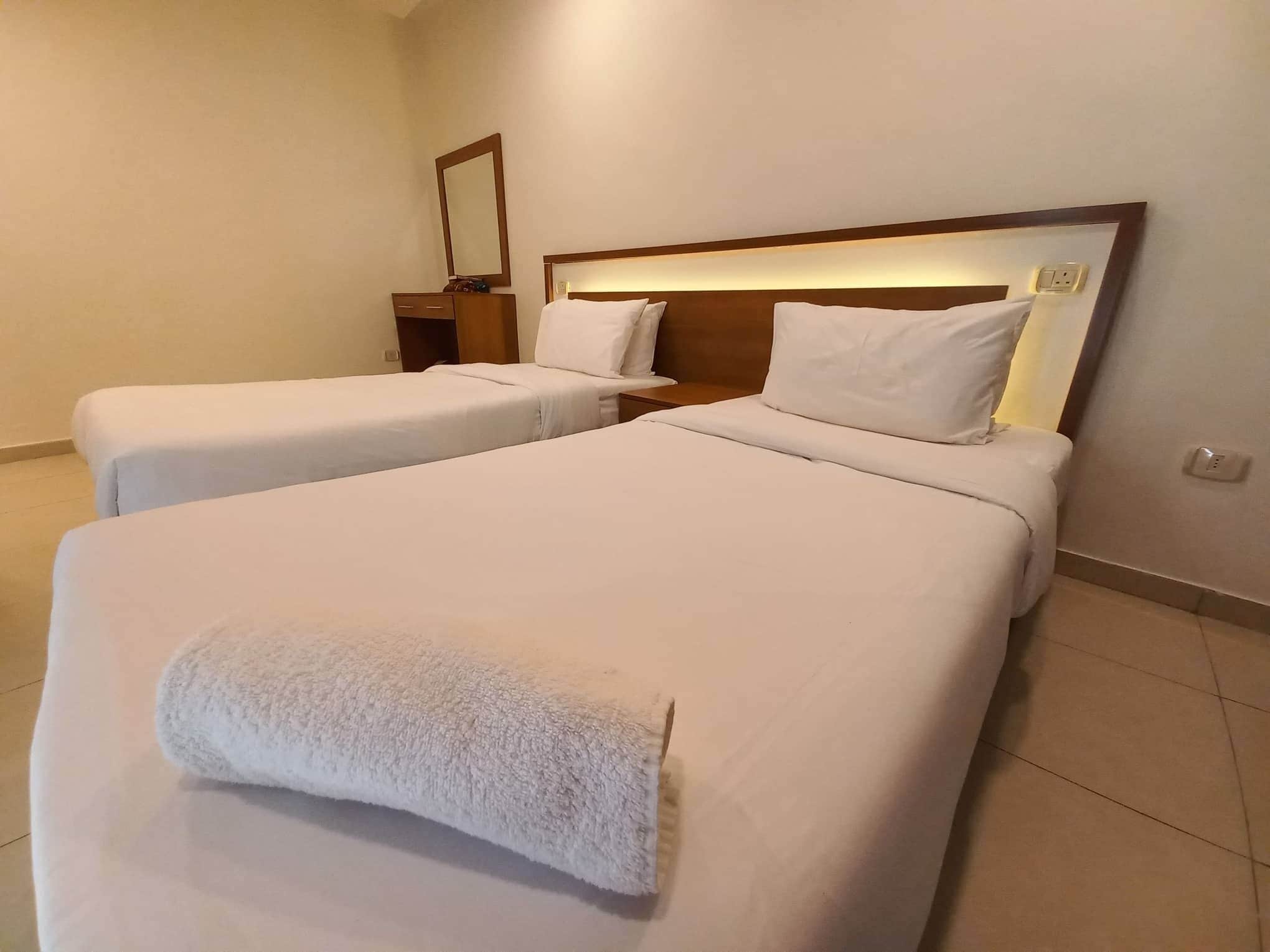 A hotel room with two single beds, a nightstand, a mirror, and a wall socket.