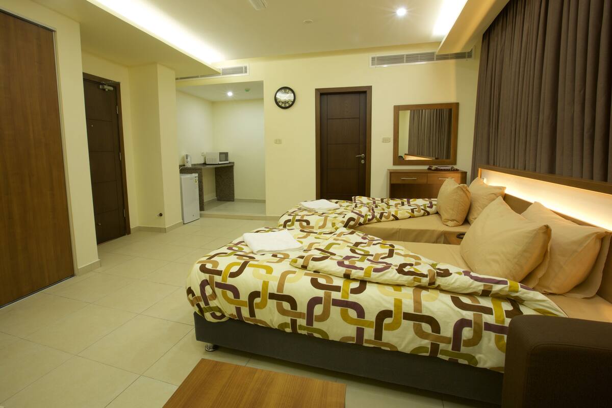 A hotel room with a bed, a desk, a mirror, and a door.