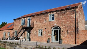 A brick building with a red-tiled roof, a staircase leading to a balcony, and a door with a small window. - The Gables - 2 bedroom self catered cottage apartment (BARNETBY)