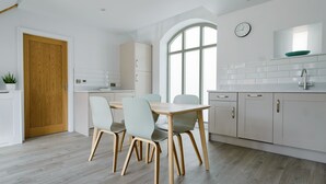A modern kitchen with a wooden dining table and chairs, white cabinets, and a large window. - The Gables - 2 bedroom self catered cottage apartment (BARNETBY)