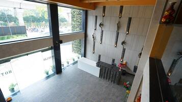 A hotel reception area with a modern design, including a reception desk, a wall with decorative elements, and a view of the street outside.