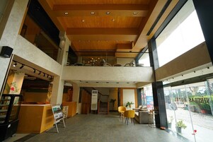 Un vestíbulo de hotel con techo de madera, una recepción, una escalera y una zona de estar con sillas amarillas.