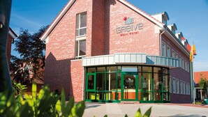 Un bâtiment en briques rouges, avec une entrée verte et le nom « GREIVE » inscrit sur la façade.