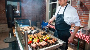 Un chef prépare différents types de viande et de légumes sur un grill, à l’extérieur.