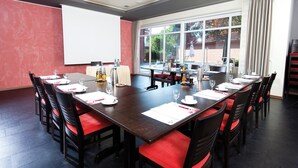 Une salle de conférence dotée d’une longue table, de chaises rembourrées de couleur rouge, d’un écran de projection et offrant une vue sur l’extérieur grâce à de grandes fenêtres.