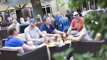 A group of people dining outdoors at a restaurant with wicker furniture and a table set with food and drinks.
