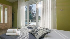 A bedroom with a bed, pillows, a wardrobe, and a sliding glass door leading to a balcony.