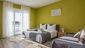A hotel room with a large bed, a smaller bed, a balcony with a pool, and a painting on the wall.