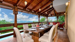 Un espace extérieur abrité, aménagé pour les repas, avec une table en bois prévue pour quatre personnes, entourée de chaises, et offrant une vue sur un paysage pittoresque.