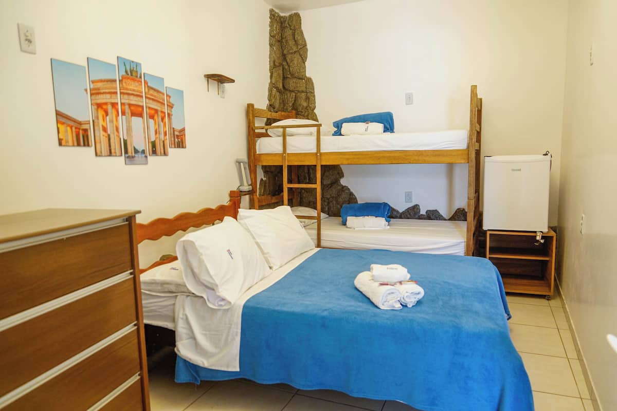 A room with bunk beds, a dresser, a wall-mounted shelf, and a whiteboard.