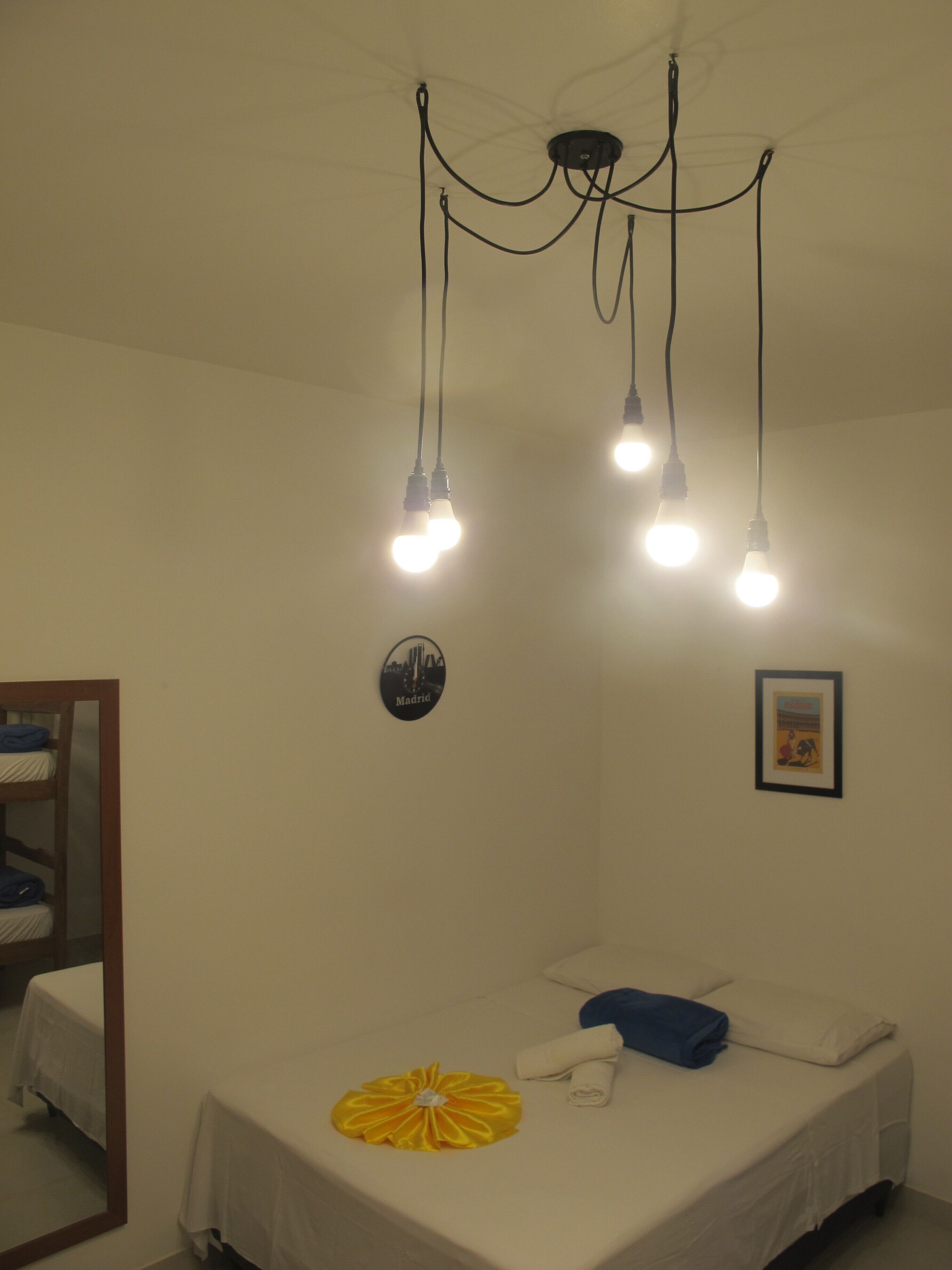 Una cama individual con una flor amarilla, ropa de cama blanca y una almohada azul. Hay tres lámparas en el techo.