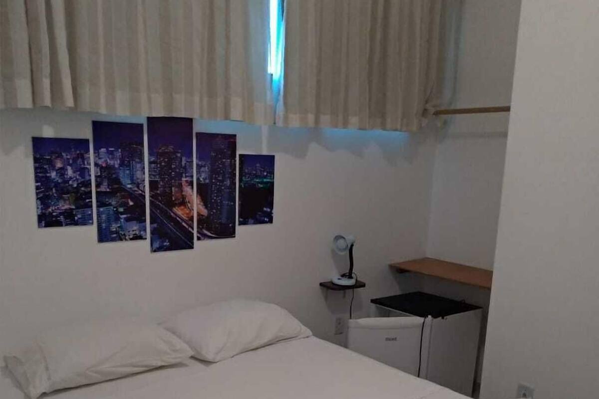 A hotel room with a bed, a nightstand, a mirror, and a window with curtains.
