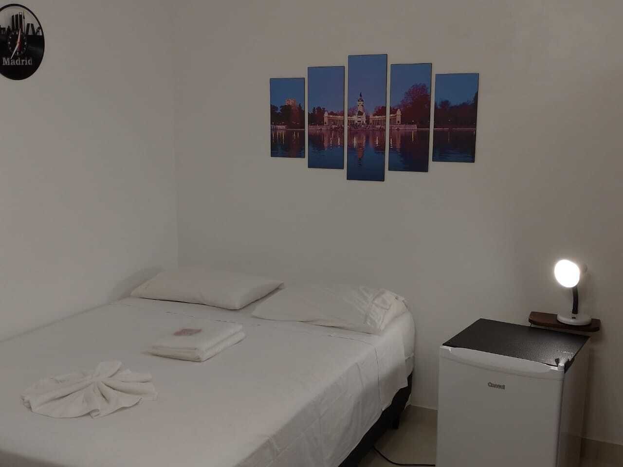 Ein Schlafzimmer mit einem Bett, einem Nachttisch mit Lampe und einem an der Wand hängenden Stadtbild.