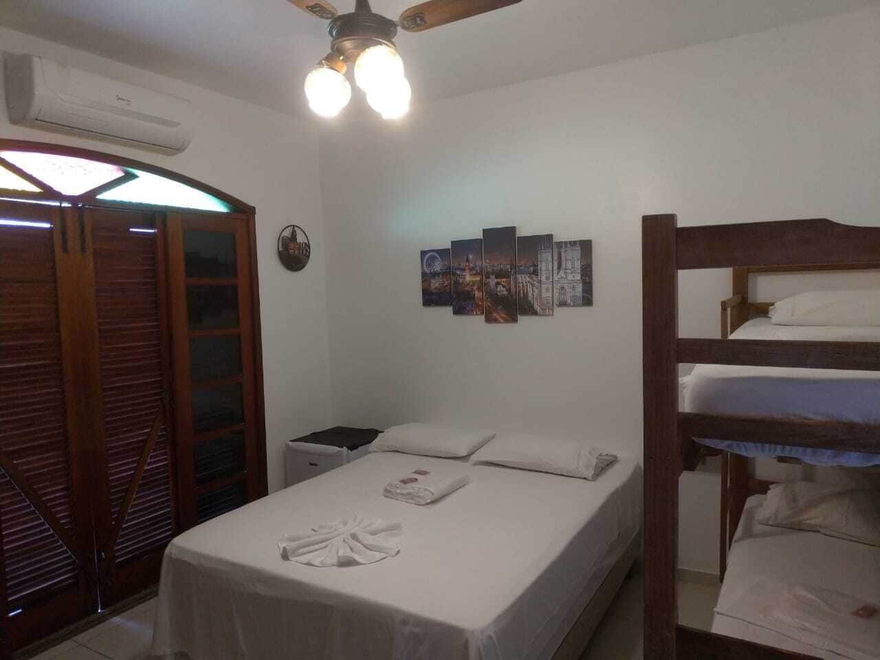 A bedroom with a bunk bed, a single bed, a nightstand, a wall-mounted air conditioner, and a ceiling fan.