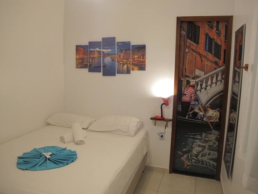 A hotel room with a bed, a wall-mounted artwork depicting a cityscape, a night lamp, and a door with a mural.