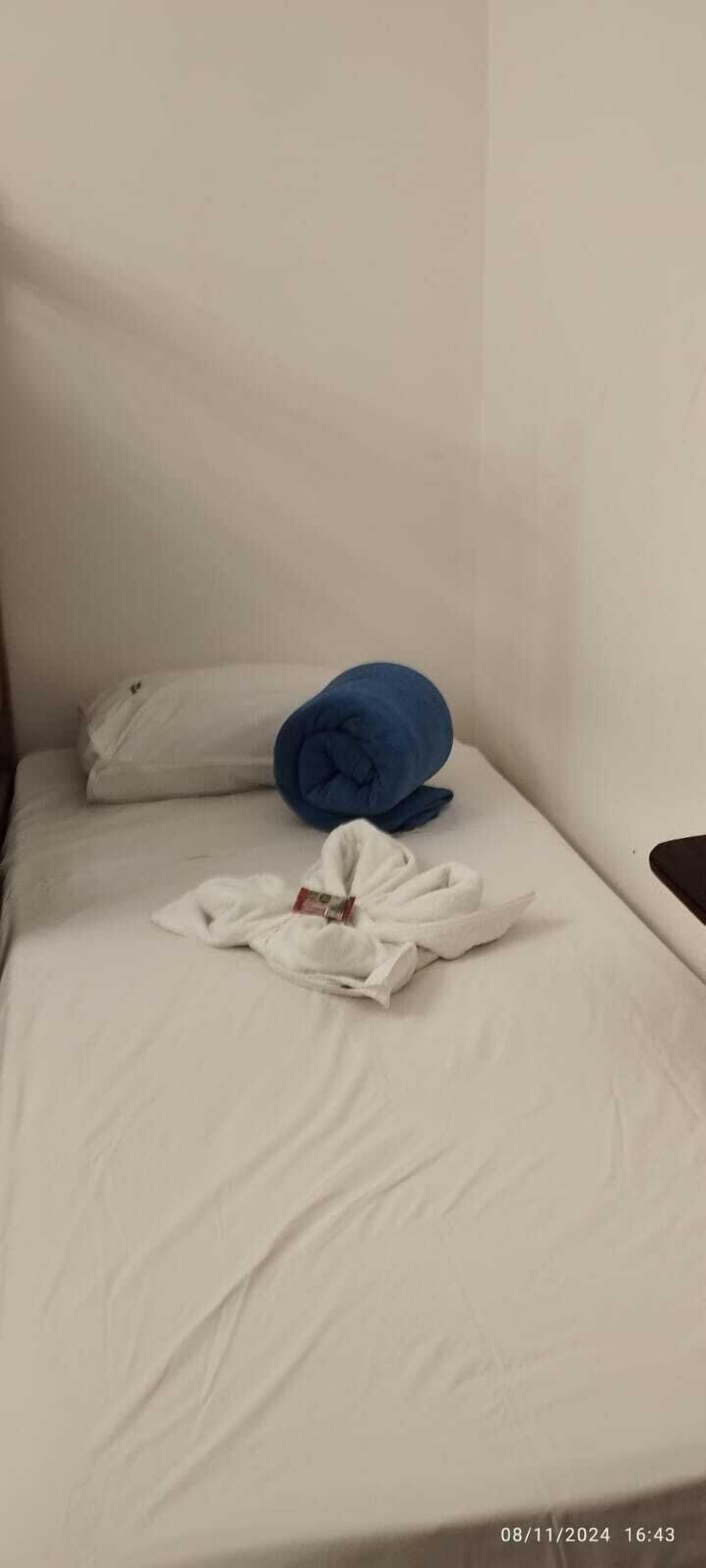 Uma cama de solteiro com lençol branco, travesseiro azul e toalha branca sobre a cama.