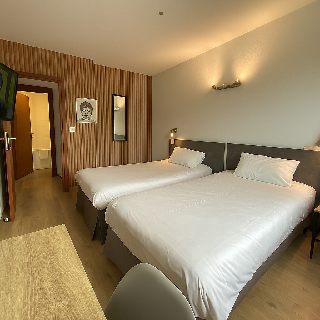 A hotel room with two beds, a wooden panel wall, a framed portrait, and a small table.