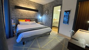 A modern hotel room with a large bed, a desk, and a bathroom visible through an open door. - Savoie Hotel (Saint-Julien-en-Genevois)