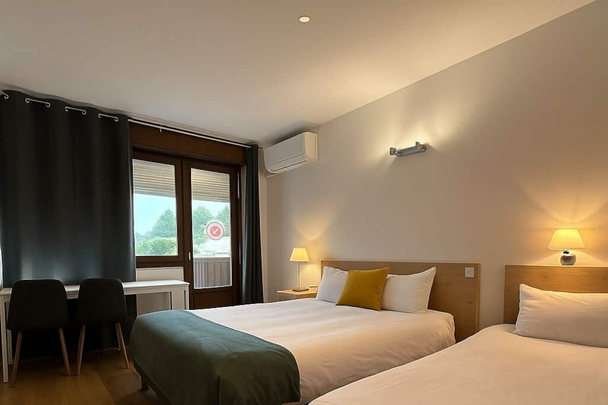 Une chambre d’hôtel avec deux lits, un bureau et une fenêtre avec des rideaux.