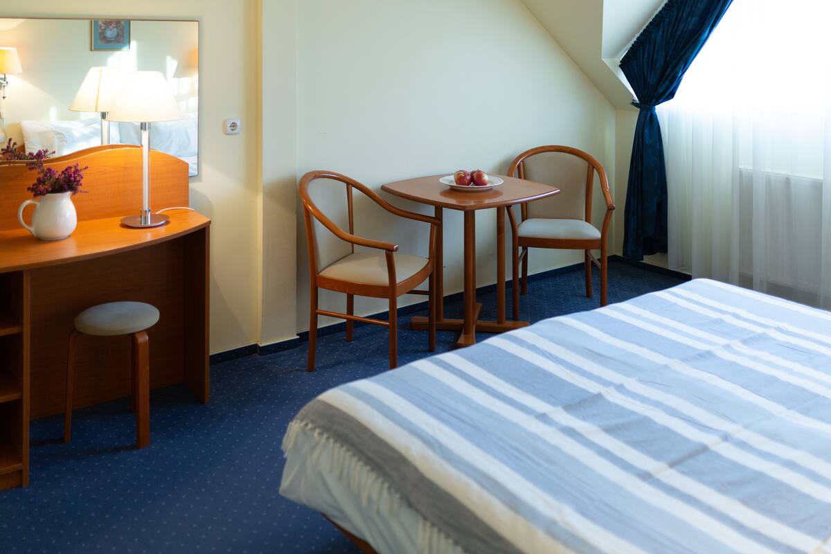 Una habitació d'hotel amb un llit, una taula de treball amb una làmpada, dues cadires i una taula petita amb pomes.
