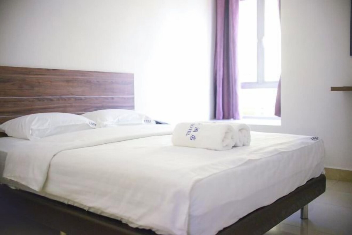 A neatly made bed with white linens, a wooden headboard, and a window with curtains.