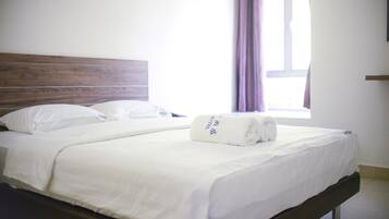 A neatly made bed with white linens and a rolled towel on the footboard.