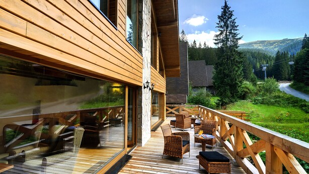 Terraza de madera con muebles de mimbre, con vista a un paisaje montañoso.