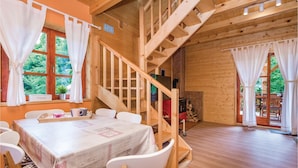 A wooden cabin interior with a dining table, chairs, a staircase, and a fireplace.