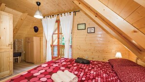 A cozy wooden cabin bedroom with a bed, a hanging light, and a window with curtains.