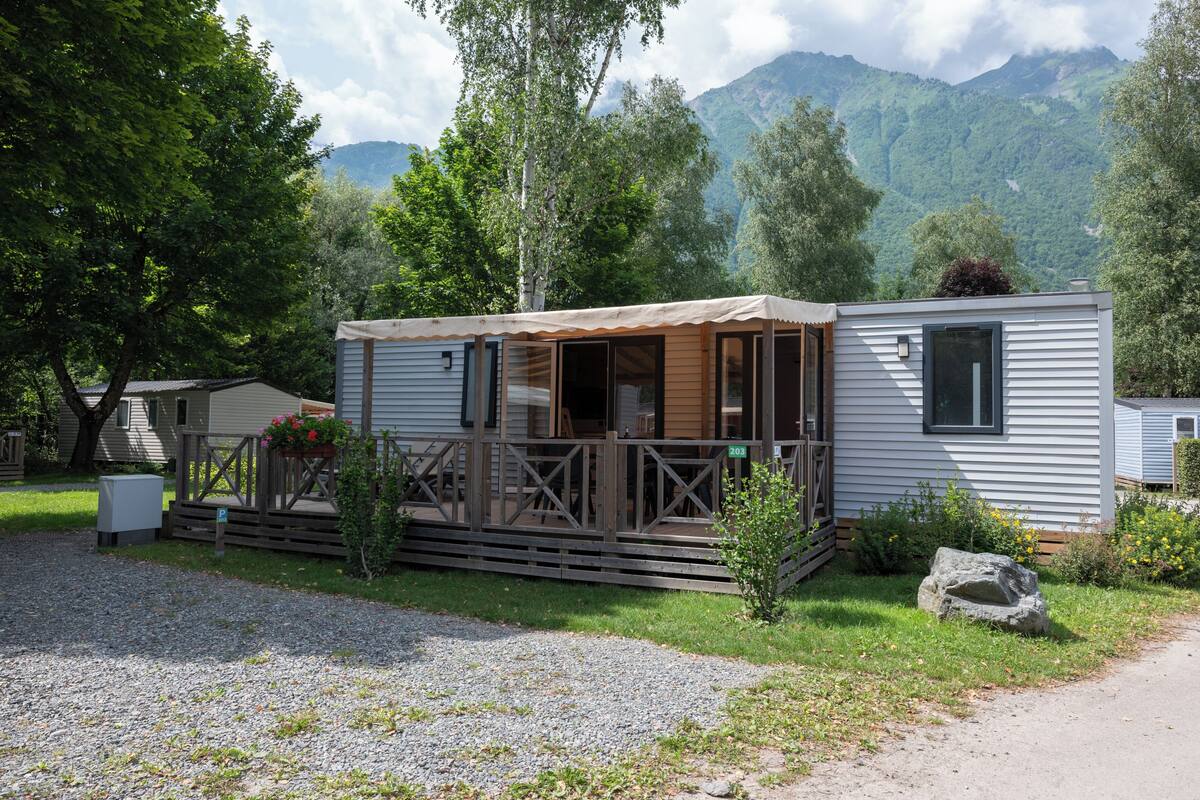 A small, single-story cabin with a porch, surrounded by trees and a mountain backdrop.